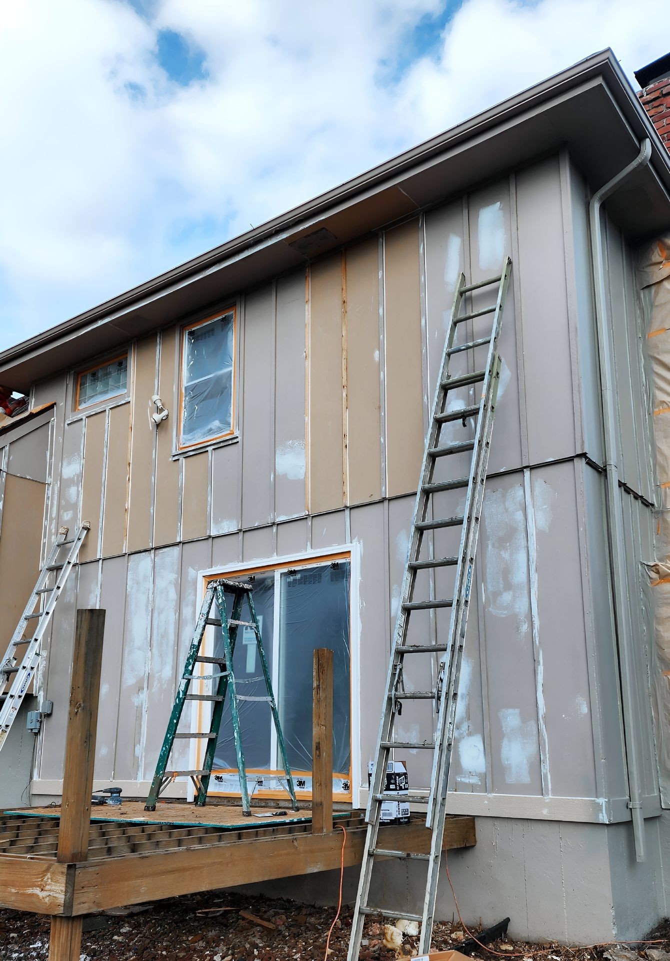 Exterior view of a house under renovation with ladders and scaffolding in place.